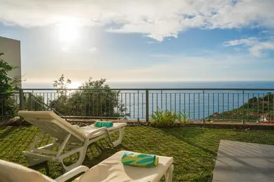 a patio with a white chair and a view of the ocean at OurMadeira - Amaro Sol in Calheta