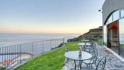 a patio with tables and chairs overlooking the ocean at Socalco Nature Calheta in Calheta