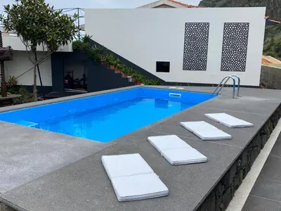 a swimming pool with two white lounge chairs in front of a house at Cottage Quinze & Apartment with Swimming pool in Ponta Delgada