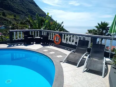 a swimming pool with two chairs and the ocean at Arcos Grand Suites with pool in Calheta