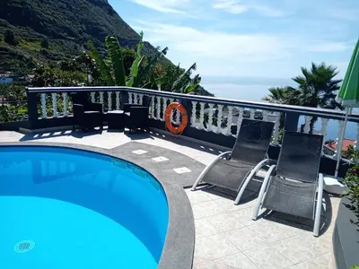 a swimming pool with two chairs and the ocean at Arcos Grand Suites with pool in Calheta