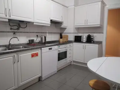 a kitchen with white cabinets and a sink and a table at Lido Funchal Apartment balcony sea view in Funchal