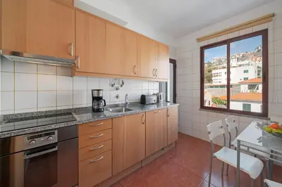 a kitchen with wooden cabinets and a table and a window at Garajau IV by An Island Apart in Caniço