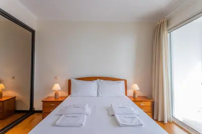 a bedroom with a bed with white sheets and a large window at FLH Funchal Balcony Apartment with Sea View in Funchal