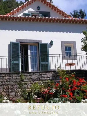 a white house with green windows and a stone wall at Refúgio das Camélias in Santana