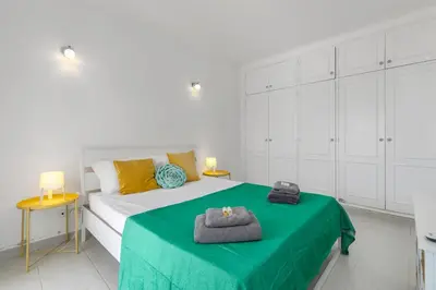 a white bedroom with a bed with a green blanket at Cozy and sunny villa just some steps from the sea in Luz