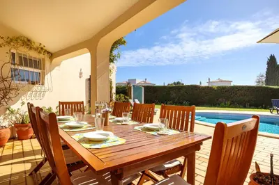 a wooden table and chairs on a patio with a pool at Villa Oceanis in Luz