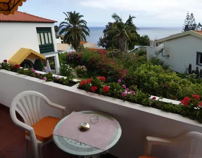 a table and chair on a balcony with flowers at Villa Erika Madeira in Caniço