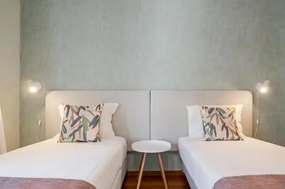two beds in a room with a table and a chair at Reis Magos IV by An Island Apart in Caniço