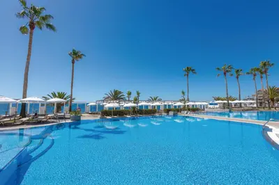 a large swimming pool with palm trees and umbrellas at Hotel Riu Madeira - All Inclusive in Caniço