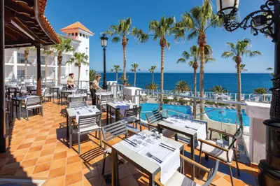 a restaurant with a pool and palm trees and the ocean at Hotel Riu Madeira - All Inclusive in Caniço
