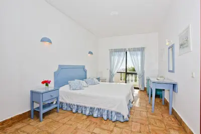 a white bedroom with a bed and a blue table at Casa dos Cardos in Luz