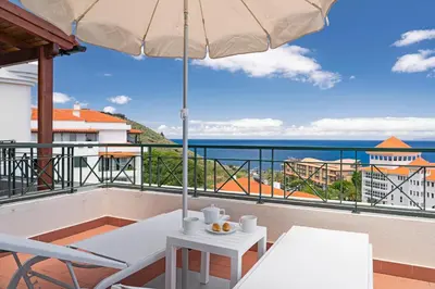 a balcony with a table and an umbrella and the ocean at Reis Magos V by An Island Apart in Caniço