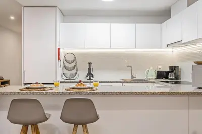 a kitchen with white cabinets and two bar stools at Funchal Tropical Apartments by Homie in Funchal