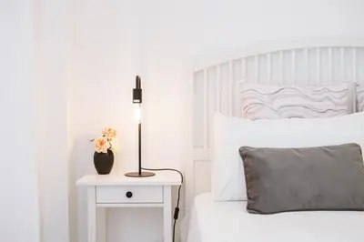 a white bedroom with a bed and a table with a lamp at Os Fragosinhos by Amazing Madeira in Funchal