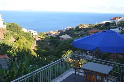 a patio with a table and an umbrella and the ocean at Descobrir Madeira in Gaula