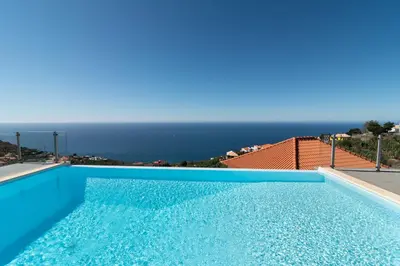a blue swimming pool with a view of the ocean at Luxo & Conforto in Calheta