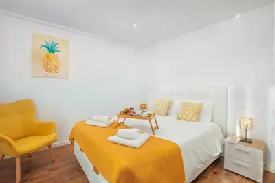 a white bedroom with a bed and a yellow chair at Golden Sea Horizon in Funchal