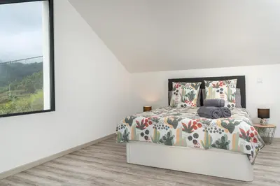 a white bedroom with a bed and a large window at Casa Zé, in Arco da Calheta