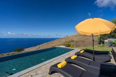 a group of chairs under an umbrella next to a swimming pool at Villa Flora - Nature & Tranquility - Heated pool optional in Jardim do Mar