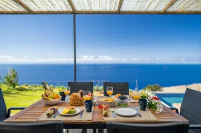 a wooden table with food and wine and a view of the ocean at Villa Flora - Nature & Tranquility - Heated pool optional in Jardim do Mar