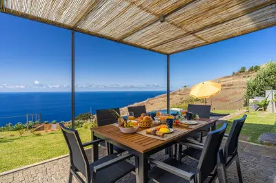 a dining table with chairs and a view of the ocean at Villa Flora - Nature & Tranquility - Heated pool optional in Jardim do Mar