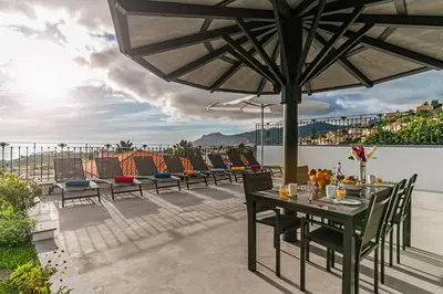 a patio with chairs and a table with an umbrella at Exquisite Madeira Villa Villa Funchal Belair 4 Bedroom Panoramic Sea View in Funchal