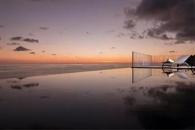 a swimming pool with a sunset in the background at Spectacular Calheta Villa Villa Cliffscape 3 Bedrooms Panoramic Sea View in Estreito da Calheta