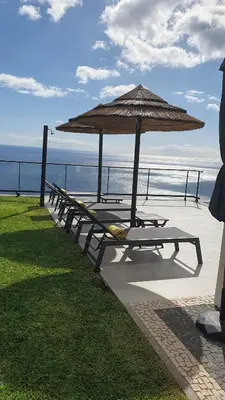 a row of benches with an umbrella and the ocean at Villa Brava Atlântico in Ribeira Brava