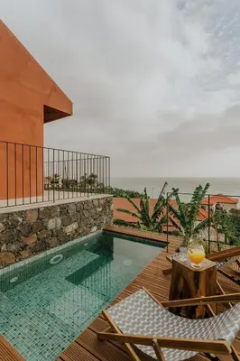 a swimming pool with two chairs and a table at Mango House in Arco da Calheta