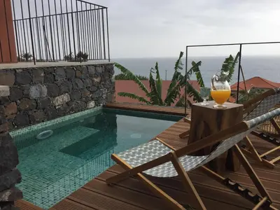 a glass of orange juice sitting on a table next to a pool at Mango House in Arco da Calheta