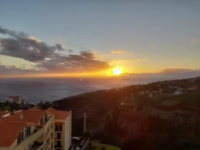a sunset over the ocean with a building at Sunset Star with Sea View in Calheta