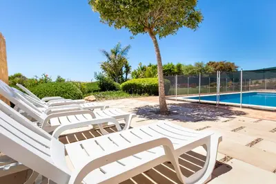 a row of white lounge chairs next to a swimming pool at Beach Villa - oceanfront villa Martinhal in Sagres