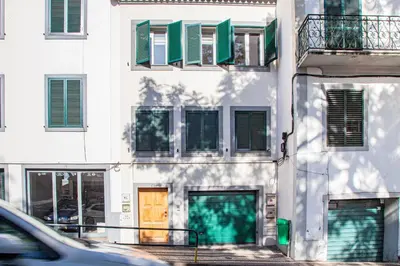 a white building with green shuttered windows and a yellow door at Harmony Apartment in Funchal
