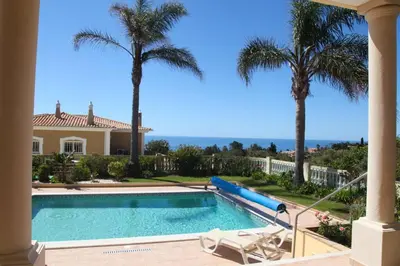 a swimming pool with palm trees and a house at Vila G, Mira Luz in Luz