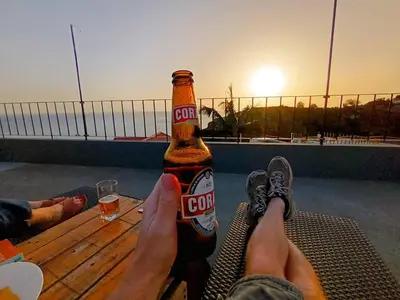 a person holding a bottle of corona beer on a table at Vаrаndаs dо Sоl-Vista relaxante entre mar e montanha in Ponta do Sol