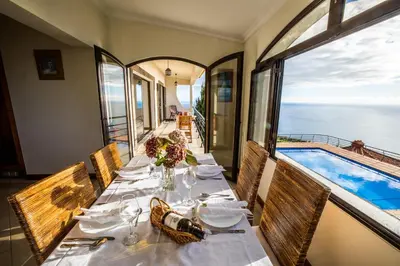a dining room with a table and a swimming pool at Secluded Sunset Villa on Cliff & 180 Degree Ocean Views in Fajã da Ovelha