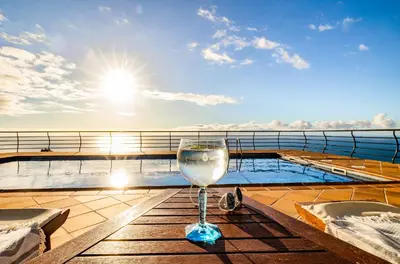 a glass of wine sitting on a table on a cruise ship at Secluded Sunset Villa on Cliff & 180 Degree Ocean Views in Fajã da Ovelha