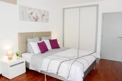 a white bedroom with a large bed with purple pillows at Sol do Lido in Funchal
