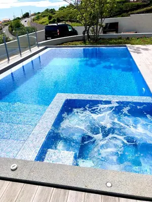 a large blue swimming pool next to a house at Villa Pinheira IV -Heated swimming pool in Calheta
