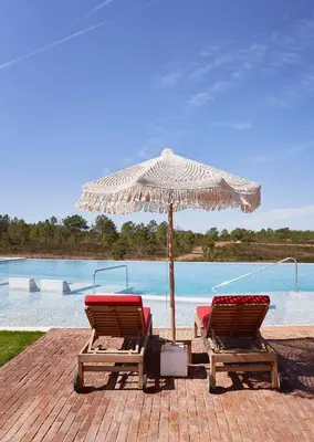 two chairs and an umbrella next to a pool at Praia do Canal Nature Retreat - Small Luxury Hotels of the World in Aljezur