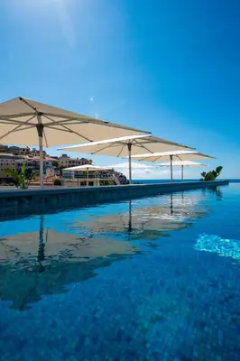 a pool of water with umbrellas on top of it at Pestana Fisherman Village in Câmara de Lobos