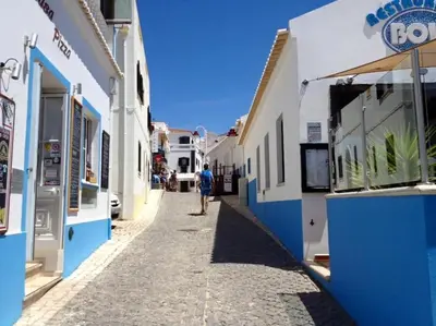 a man walking down a narrow street with buildings at Salema Beach Apartment in Salema