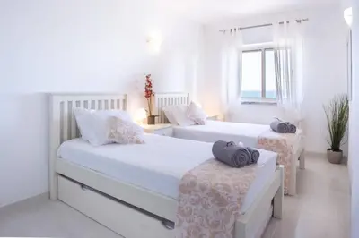 a white bedroom with two beds and a window at Apartamento Salema 33 in Salema