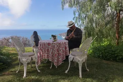 a man sitting at a table in front of the ocean at Quinta do Cabouco in Ribeira Brava