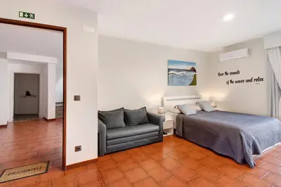 a bedroom with a bed and a chair and a mirror at Ninho Gaivota in Porto Moniz