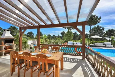a wooden table and chairs on a deck with a pool at Casa May - Spacious family home with great outdoors! in Aljezur