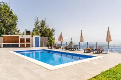 a swimming pool with chairs and umbrellas on a house at SUNNYSIDE VILLA in Calheta