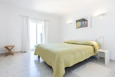 a white bedroom with a bed and a window at Paraíso dos Pássaros in Budens