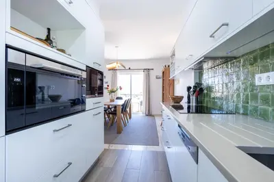a kitchen with white cabinets and a dining room at Paraíso dos Pássaros in Budens